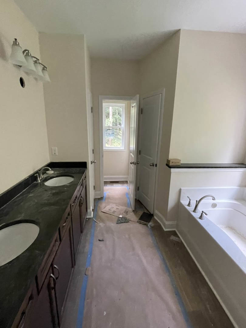 Modern bathroom with freestanding tub, white sink vanity, chrome faucet, tiled floor and walls, large window overlooking trees, row of glass light fixtures above mirror