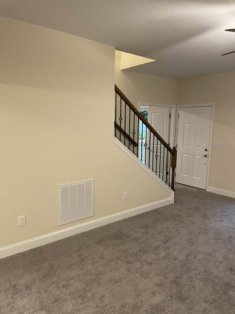 Carpeted staircase with white wooden handrail, white door with silver handle, white wall vent, and light-colored laminate flooring in a modern interior hallway