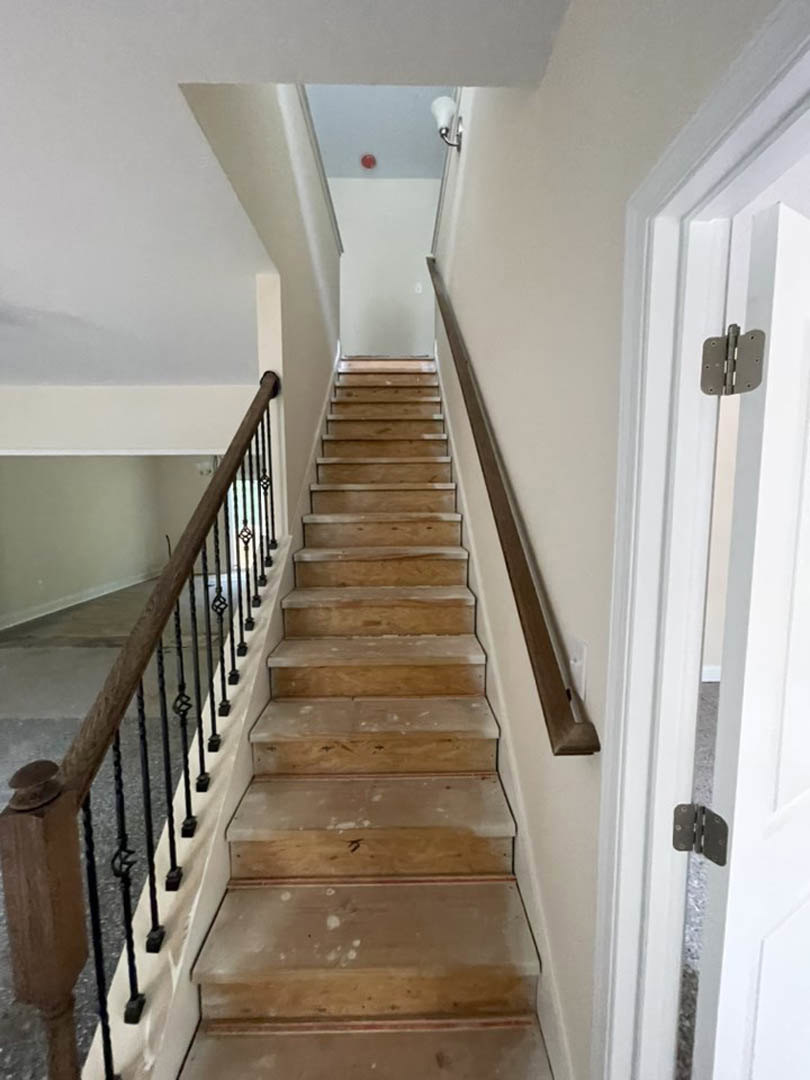 Staircase with natural wood steps and matching wood railing, white plaster walls, decorative molding along baseboards, metal balusters, and hardwood flooring