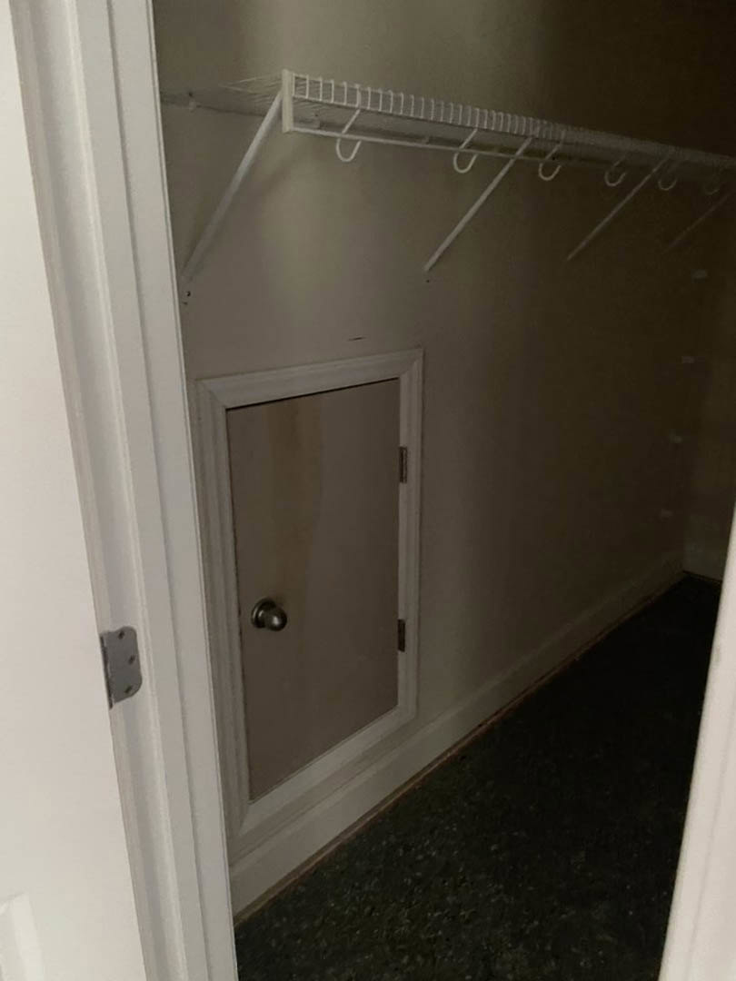White closet door open in hallway with silver knob, black flooring, white curtain rod with hooks, and black knob on gray surface