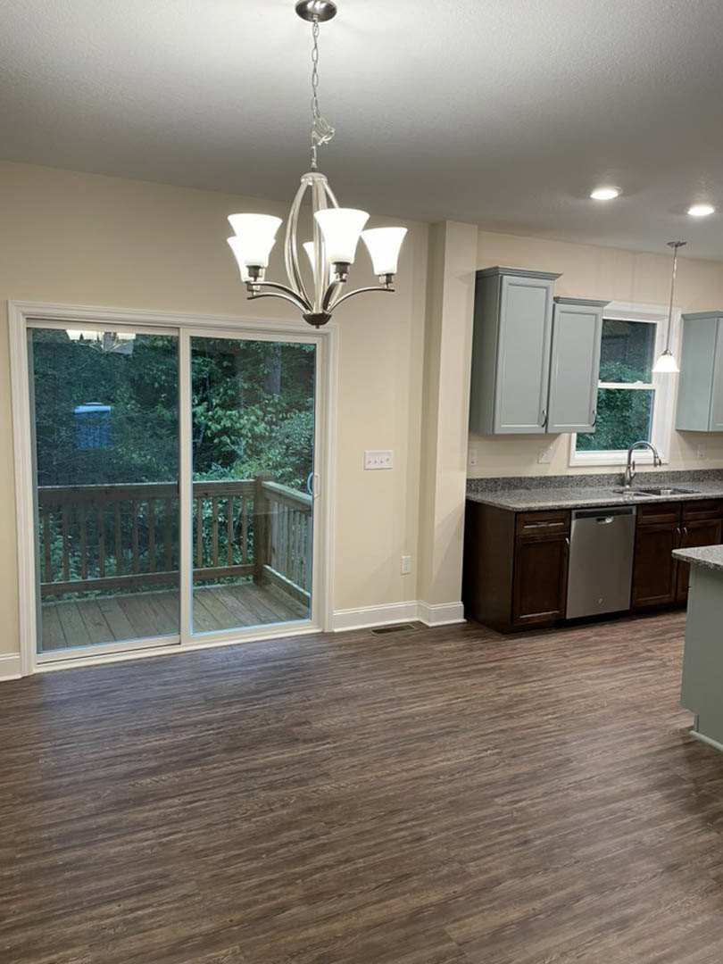 Kitchen with wood flooring, white cabinetry, sliding glass door opening to wooden deck with railing, modern chandelier overhead, black-handled appliance on countertop
