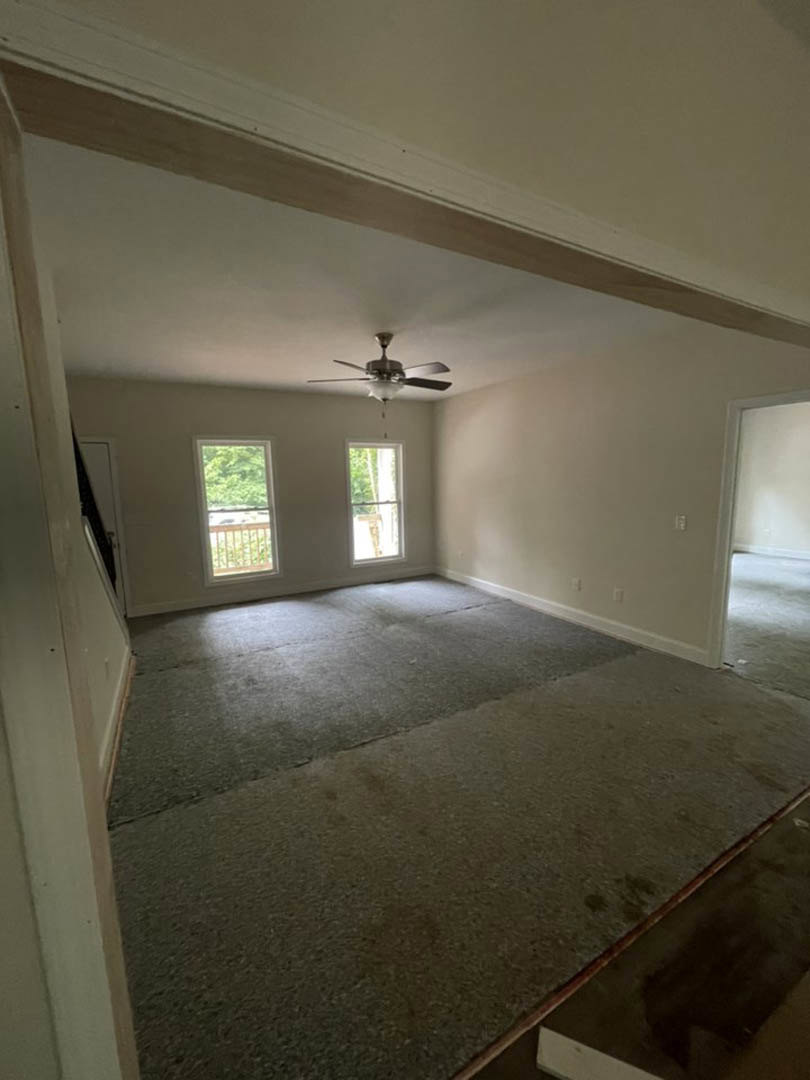 Ceiling fan with light fixture, white walls and trim, tile flooring, large window with white frame overlooking trees and railing