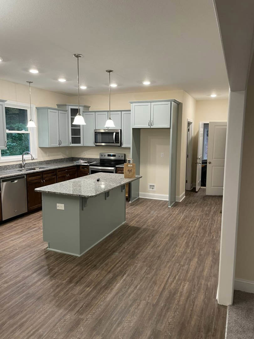 Kitchen with wood flooring, central island featuring marble countertop, white cabinetry, stainless steel microwave, large window providing natural light, and neutral walls.