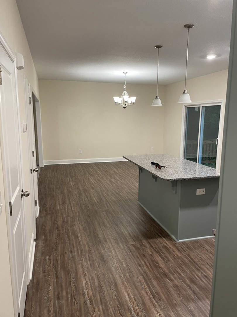 Kitchen with marble countertop, wood flooring, bar seating, white walls with black trim, sliding glass door with white frame, cabinetry, and chandelier visible in background.