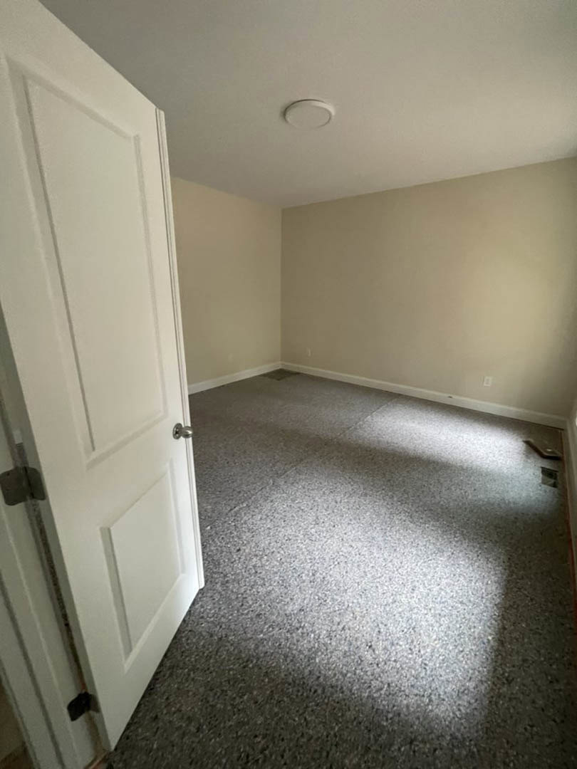 White paneled door with silver handle open onto carpeted floor, circular metal object resting on nearby surface, close-up of door hinge and hardware, plaster walls and laminate