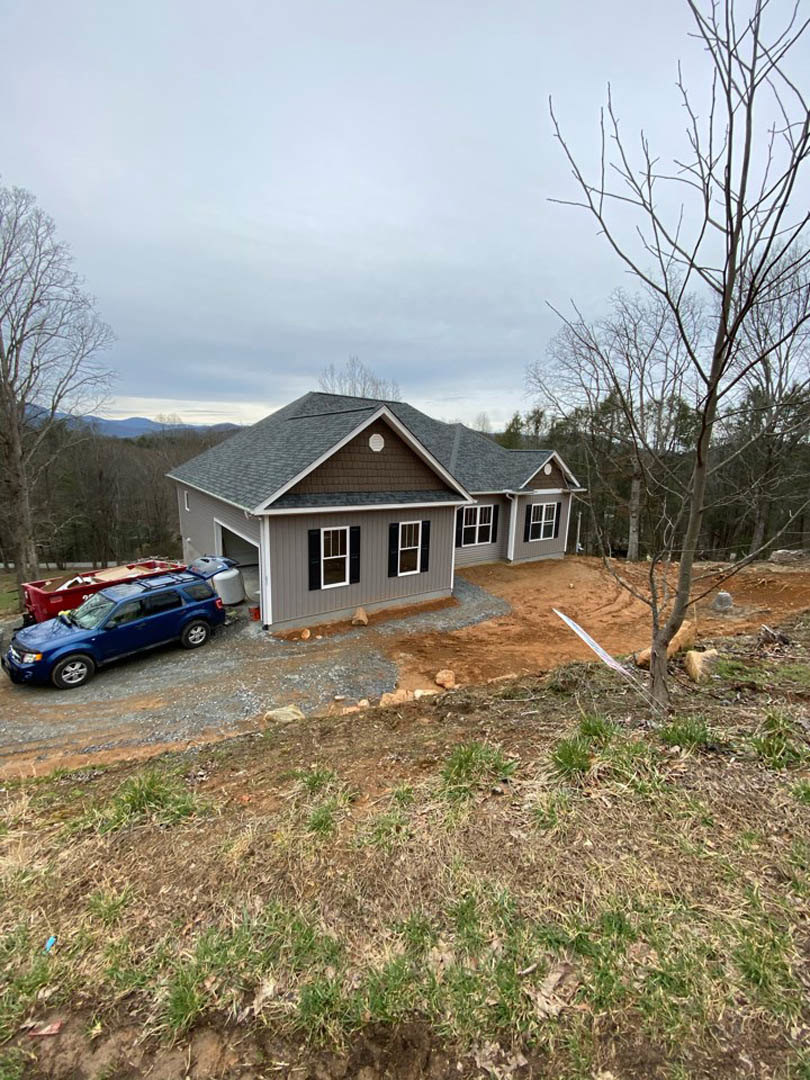 Two-story house with light siding, attached garage, leafless tree in front yard, blue pickup truck parked on driveway, red dumpster beside driveway, patchy grass, overcast sky