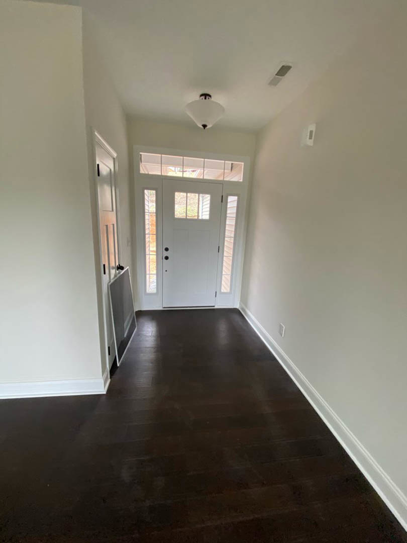 Hallway with dark wood flooring, white paneled door featuring a window, recessed ceiling light, and ceiling vent