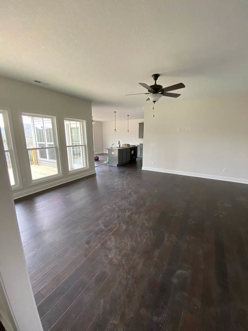 Ceiling fan with light fixture, dark stained hardwood floor, white walls, rectangular grey object, windows, and white door in a residential room