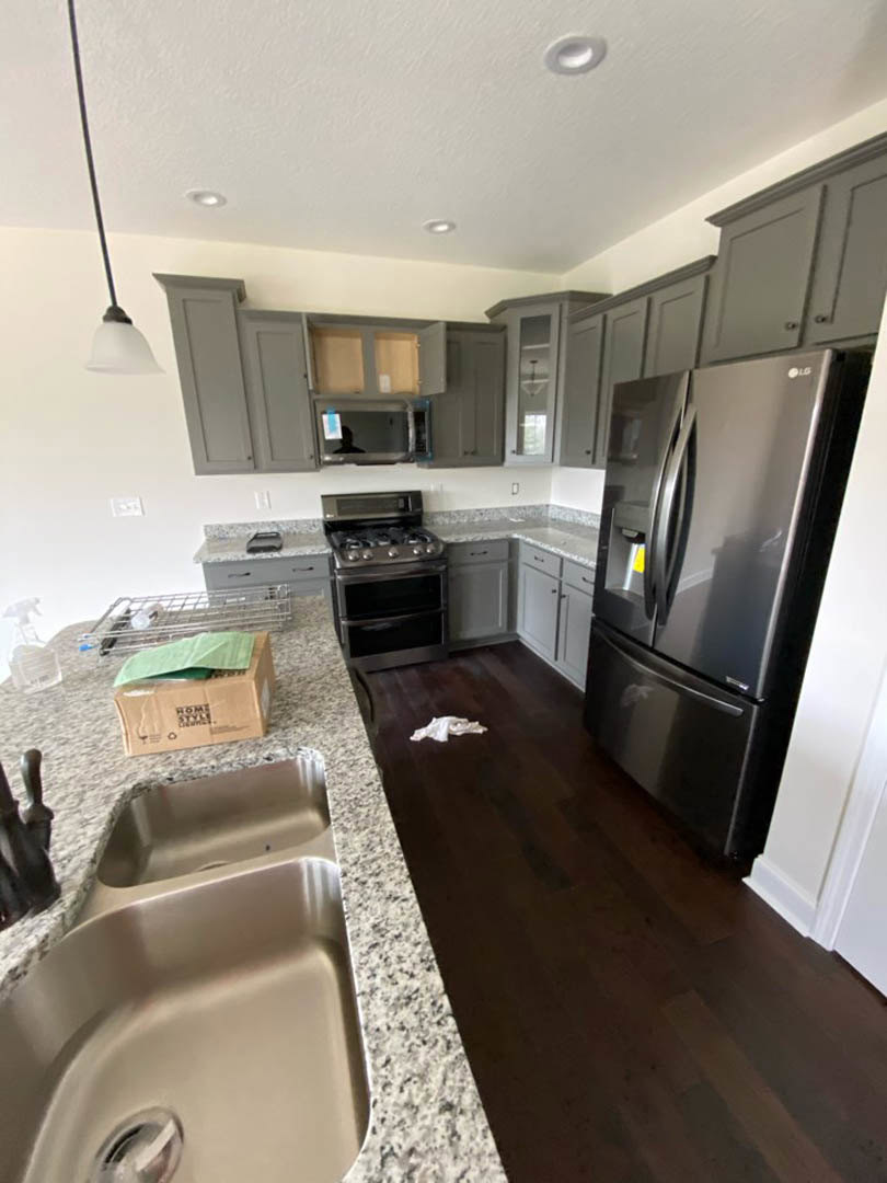 Modern kitchen with black refrigerator, stainless steel sink, white tile backsplash, light wood cabinetry, and stone countertops