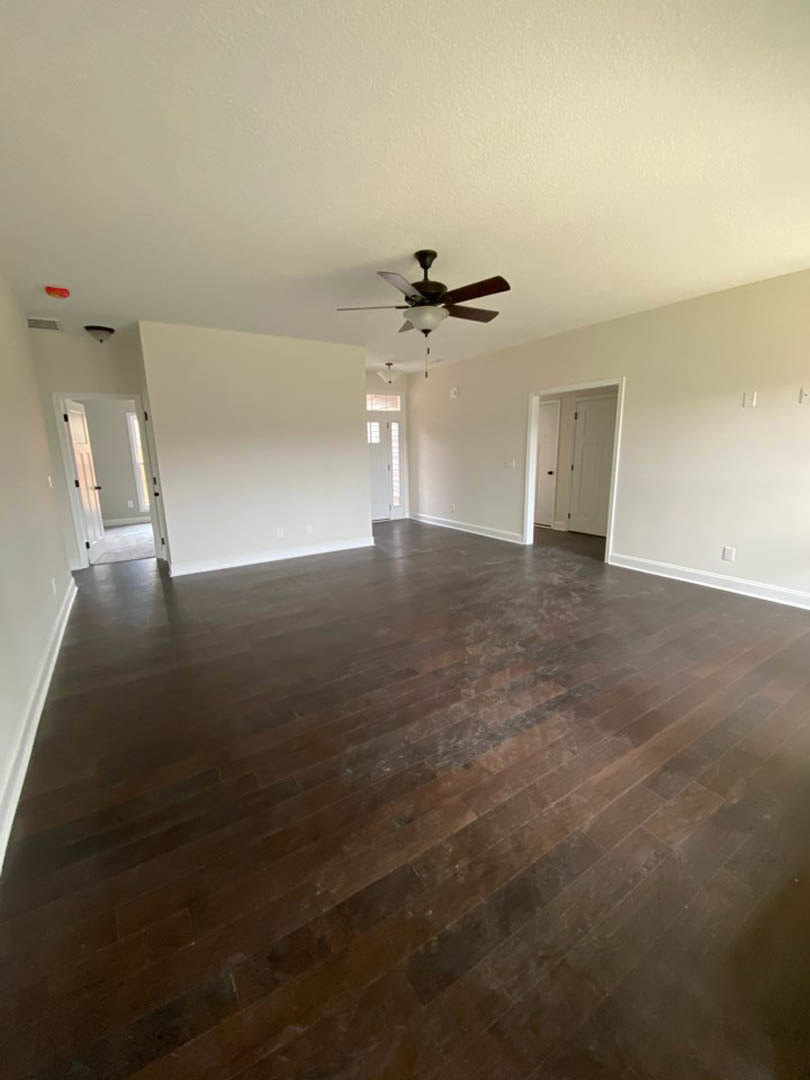 Ceiling fan with light fixture, hardwood floors, white walls, and a white door with black handle in a residential interior room