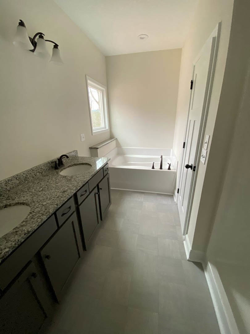 Bathroom featuring a marble countertop, freestanding bathtub, three-light fixture, white-framed window, and tile flooring.