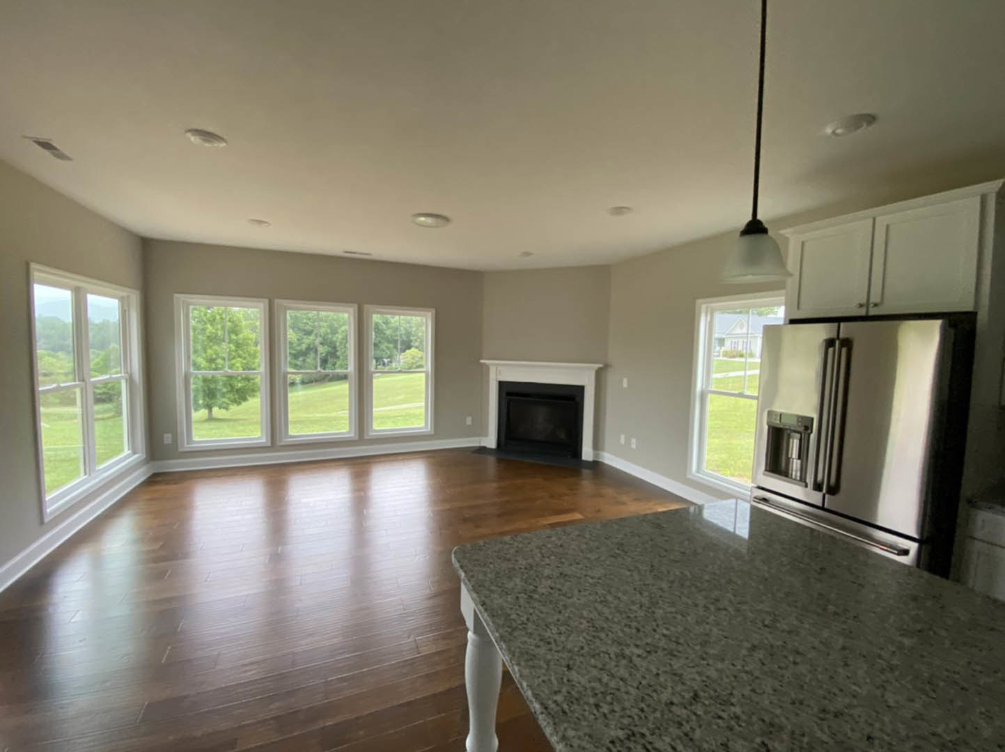 Kitchen featuring a marble island, hardwood floors, stainless steel refrigerator with water dispenser, built-in silver oven, fireplace, large windows overlooking trees