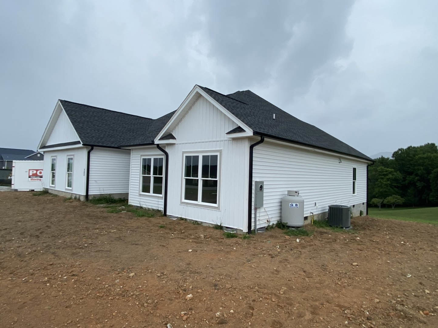 White house with black roof and white-framed windows, set on a dirt field with a grey tank and black container near the exterior.