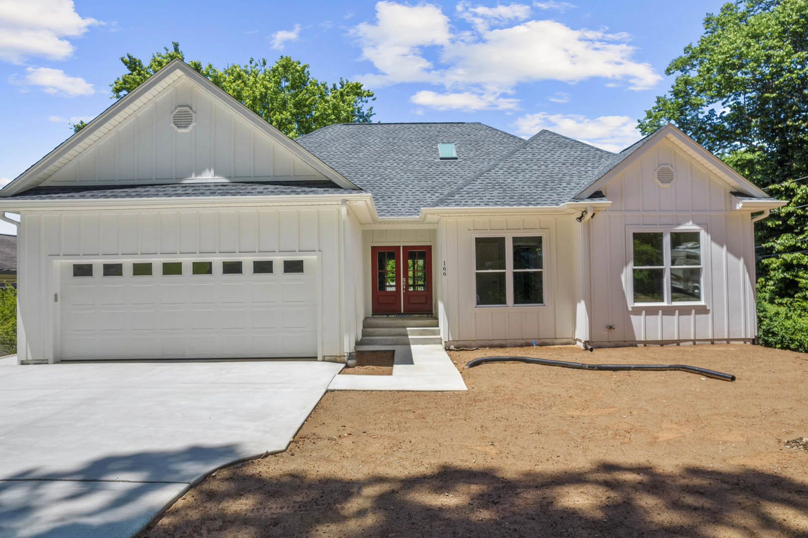 Two-story home with light siding, double red front doors with glass panes, white garage door with windows, paved driveway, and trimmed landscaping
