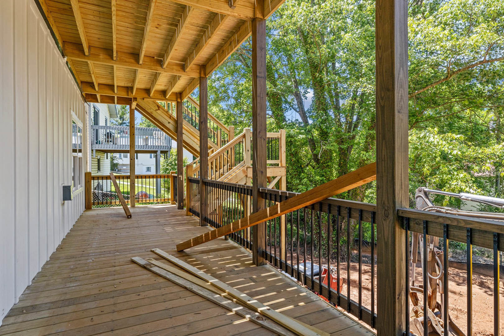 Spacious deck featuring natural wood beams, horizontal railings, and plank flooring, surrounded by mature trees providing shade.