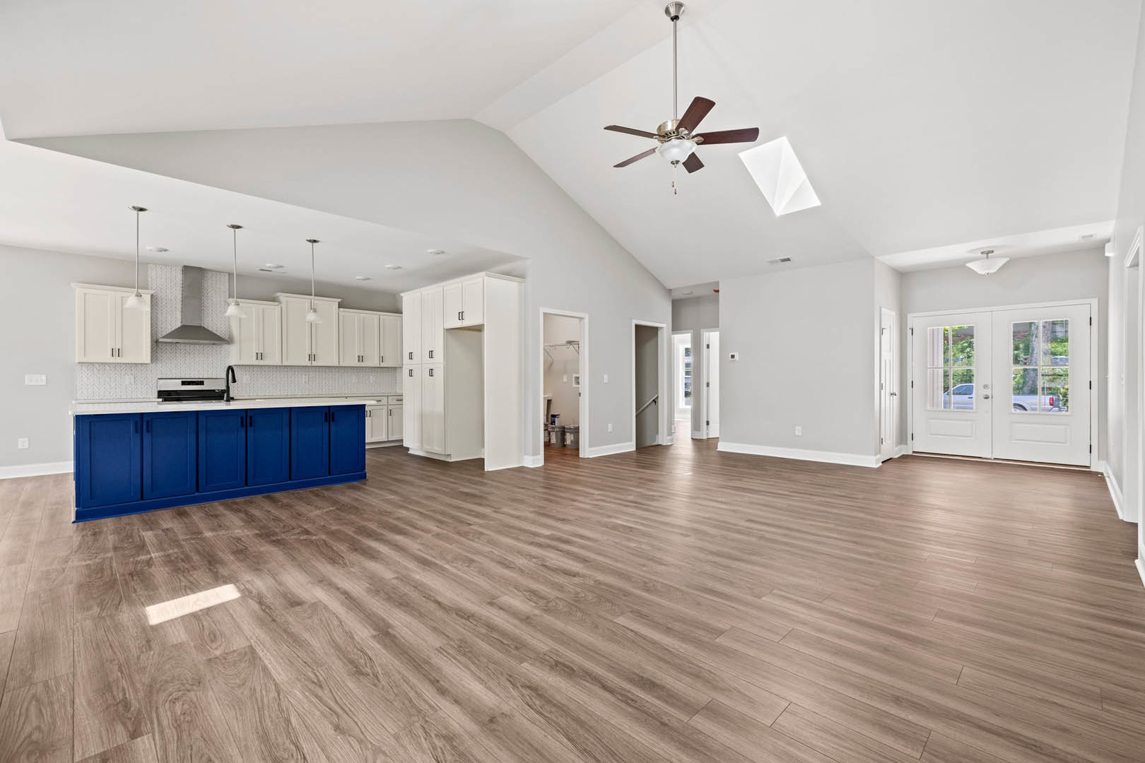 Spacious open floor plan featuring hardwood flooring, ceiling fan with light fixture, blue kitchen cabinets with white countertops, and white double doors with window panes