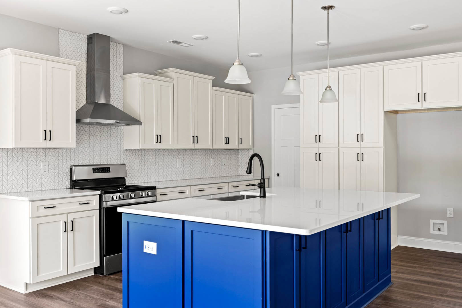 Blue kitchen island with white countertop, blue lower cabinets, stainless steel stove, white upper cabinets with black handles, white ceiling featuring round light fixture, white