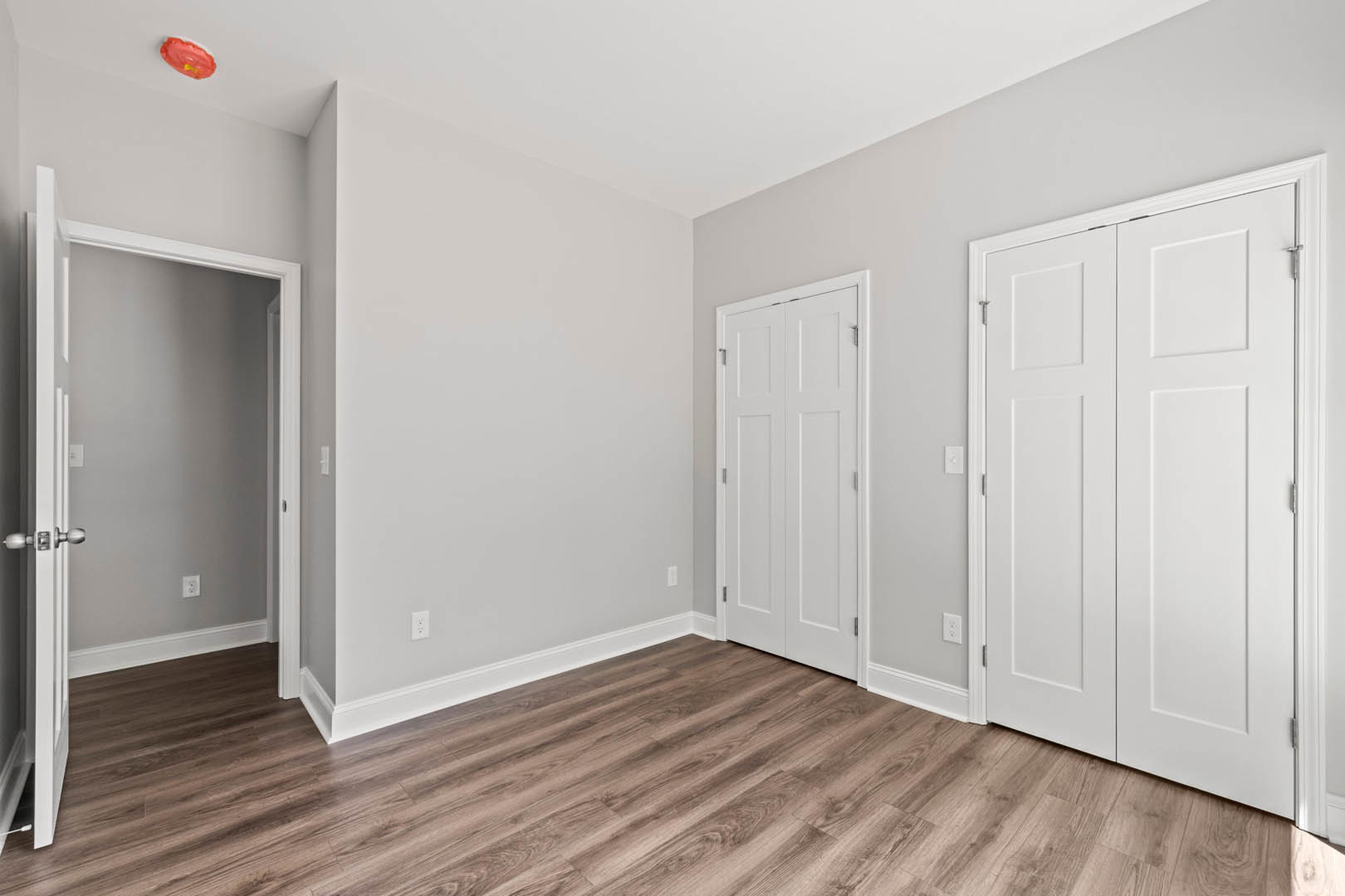 White paneled doors with silver handles, hardwood floors with white baseboard trim, open closet doors, and a red oval object with yellow center on the floor.