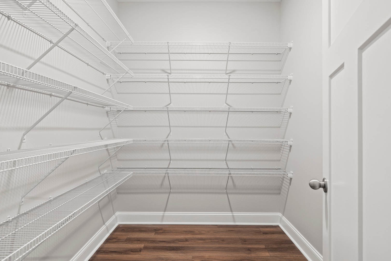 White built-in shelves along a plaster wall, wood flooring with white baseboard trim, white door with silver knob, minimalist interior.