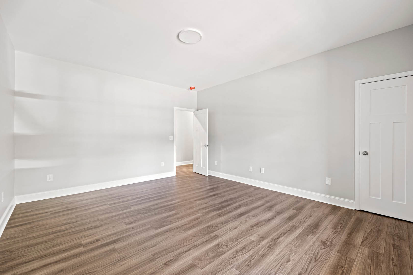 White door with silver handle open against white wall, wood laminate flooring, white ceiling with round light fixture