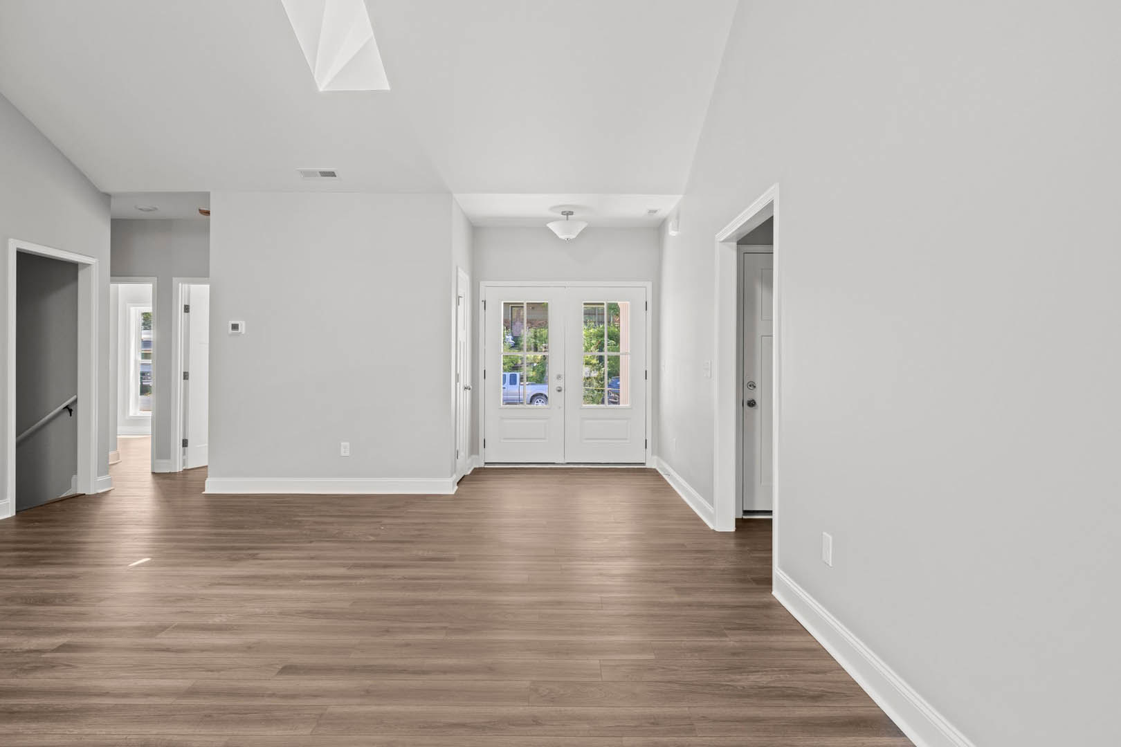 White walls, hardwood floors, double glass doors, white railing, and light switch in a bright residential interior.