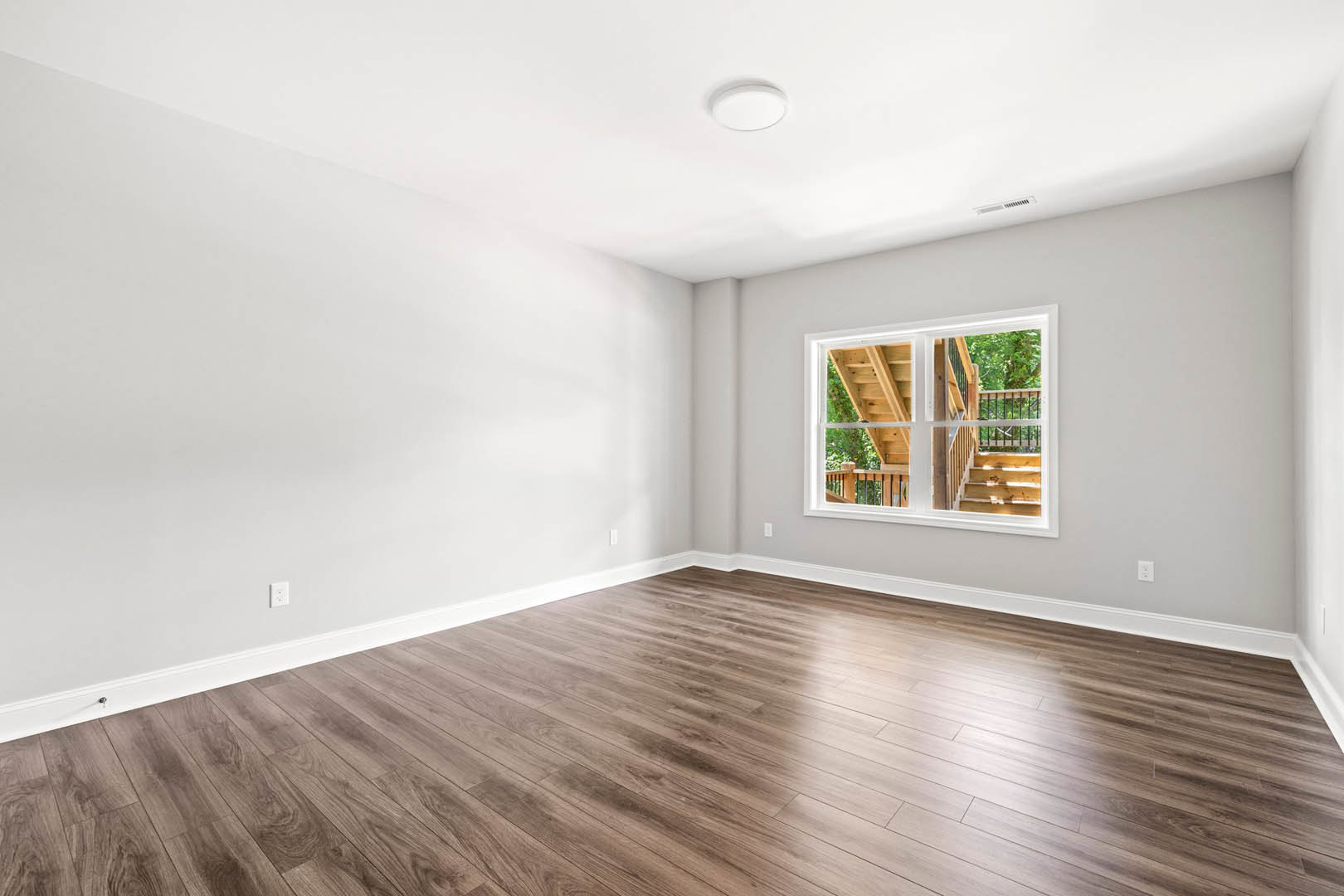 Hardwood floor room with white walls, large window overlooking wooden staircase, round ceiling light fixture with black handle