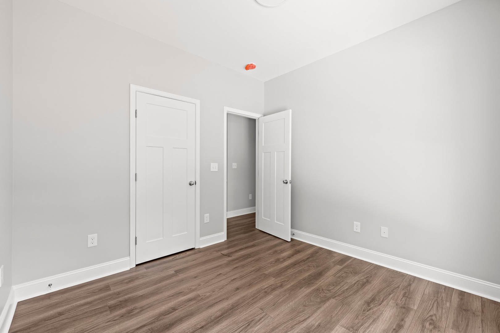 Wood flooring in a room with two white doors featuring silver knobs, white walls, and white door frames.