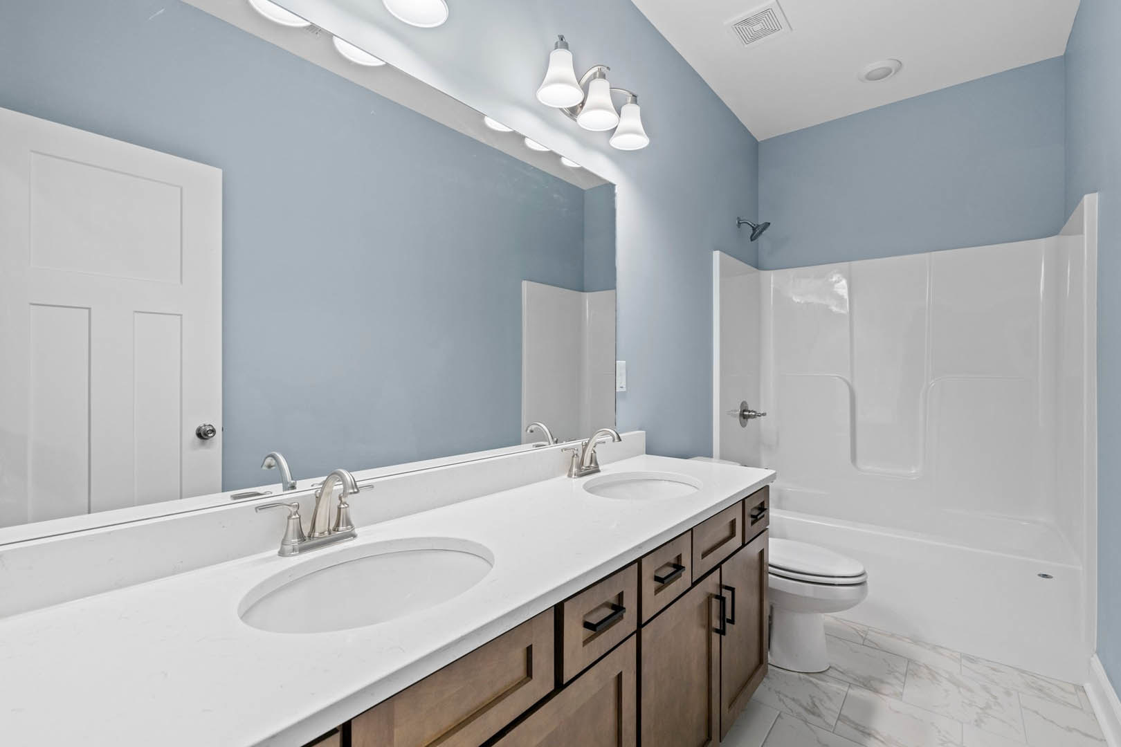 Bathroom with white toilet and sink, white door with black handle, light fixture above, tile flooring, and neutral wall finishes