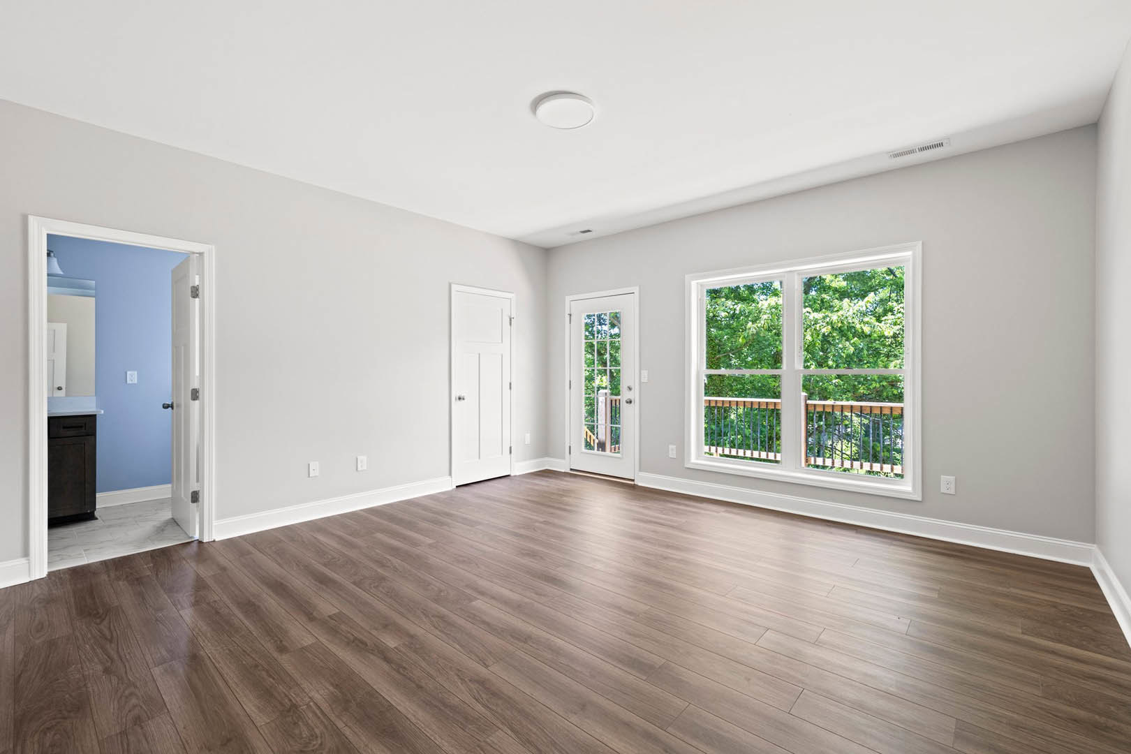Hardwood floors and white walls in a bright room with white doors, one featuring glass panes, and a window overlooking trees