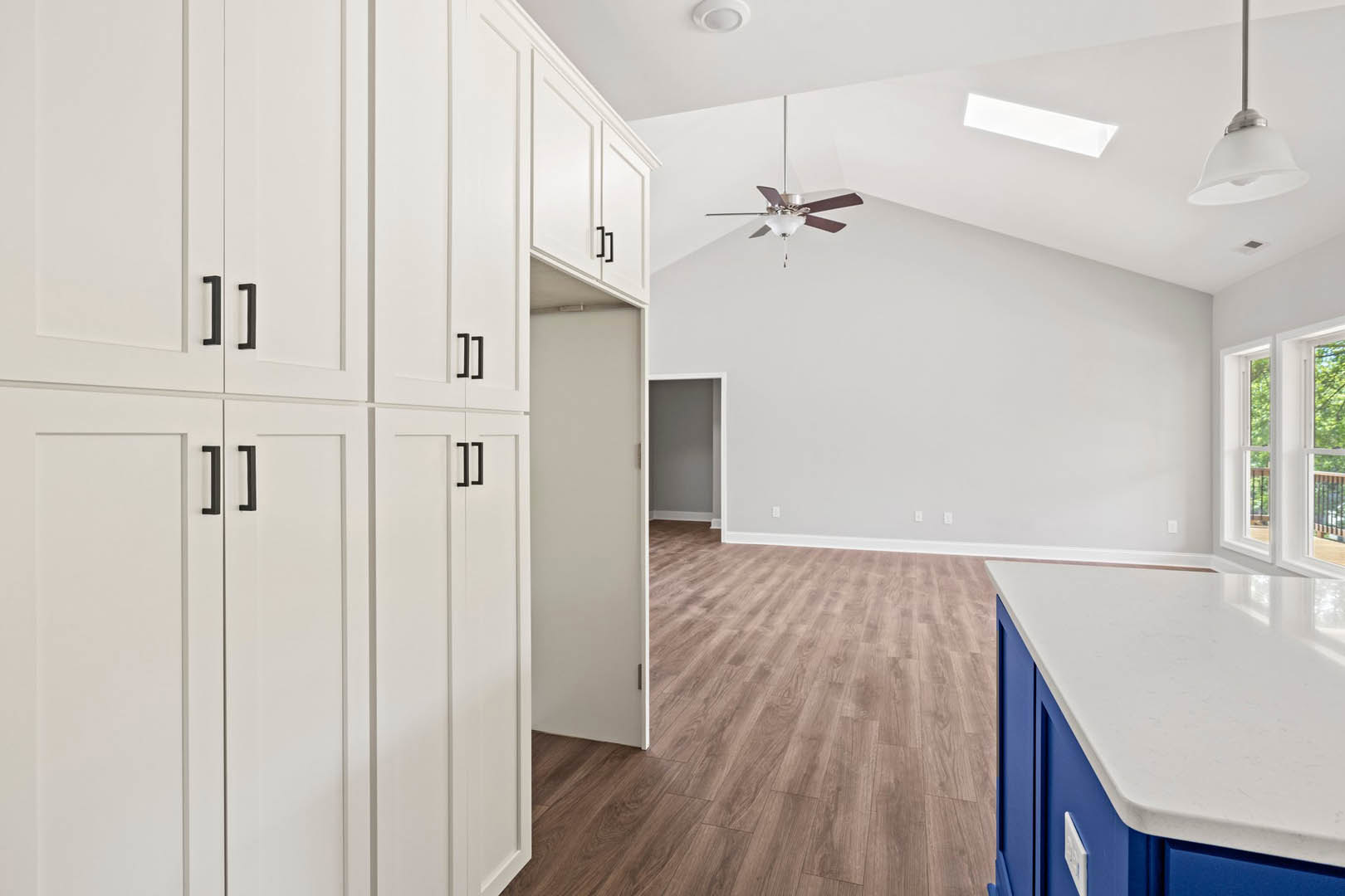 Kitchen with white cabinets, blue countertops, light wood flooring, stainless steel appliances, ceiling fan with light, white window frame overlooking balcony and trees