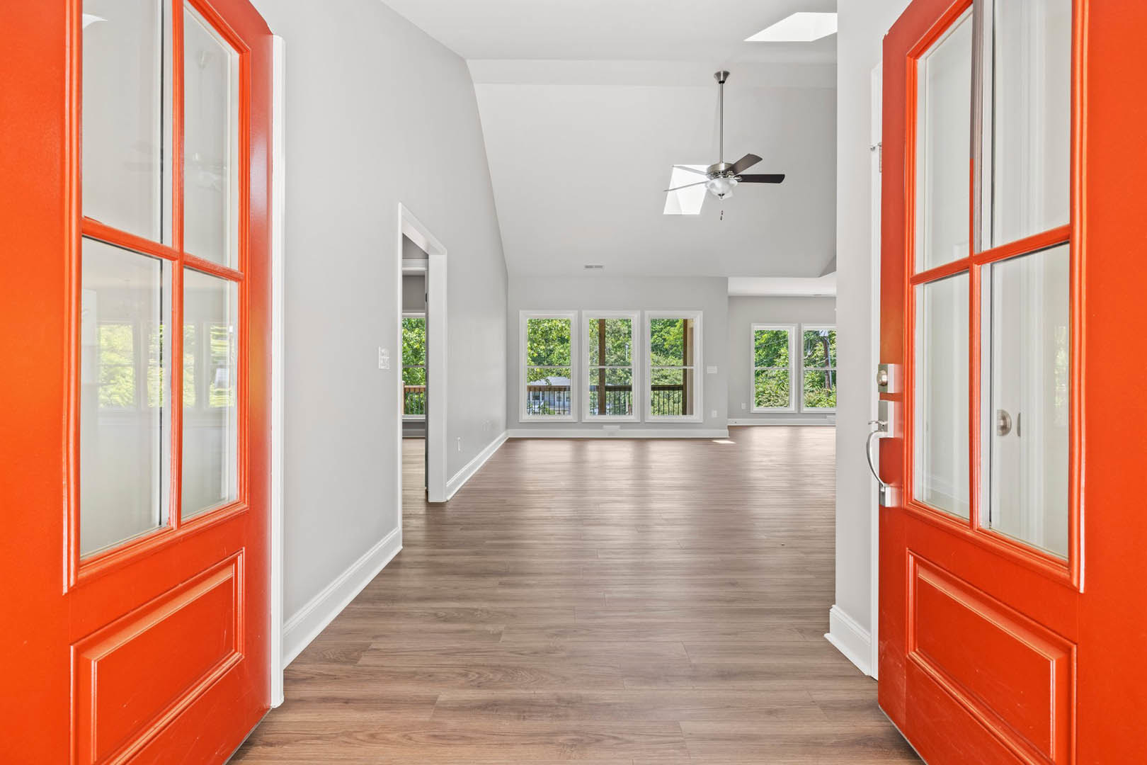 Red double doors, hardwood flooring, ceiling fan with light, large window overlooking trees, white walls
