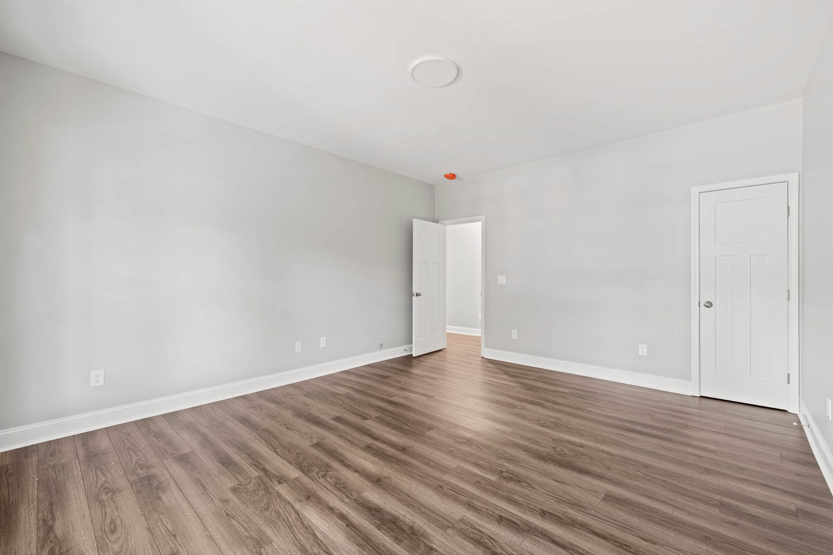 Open white door with silver knob leading into a room with wood flooring and white plaster walls