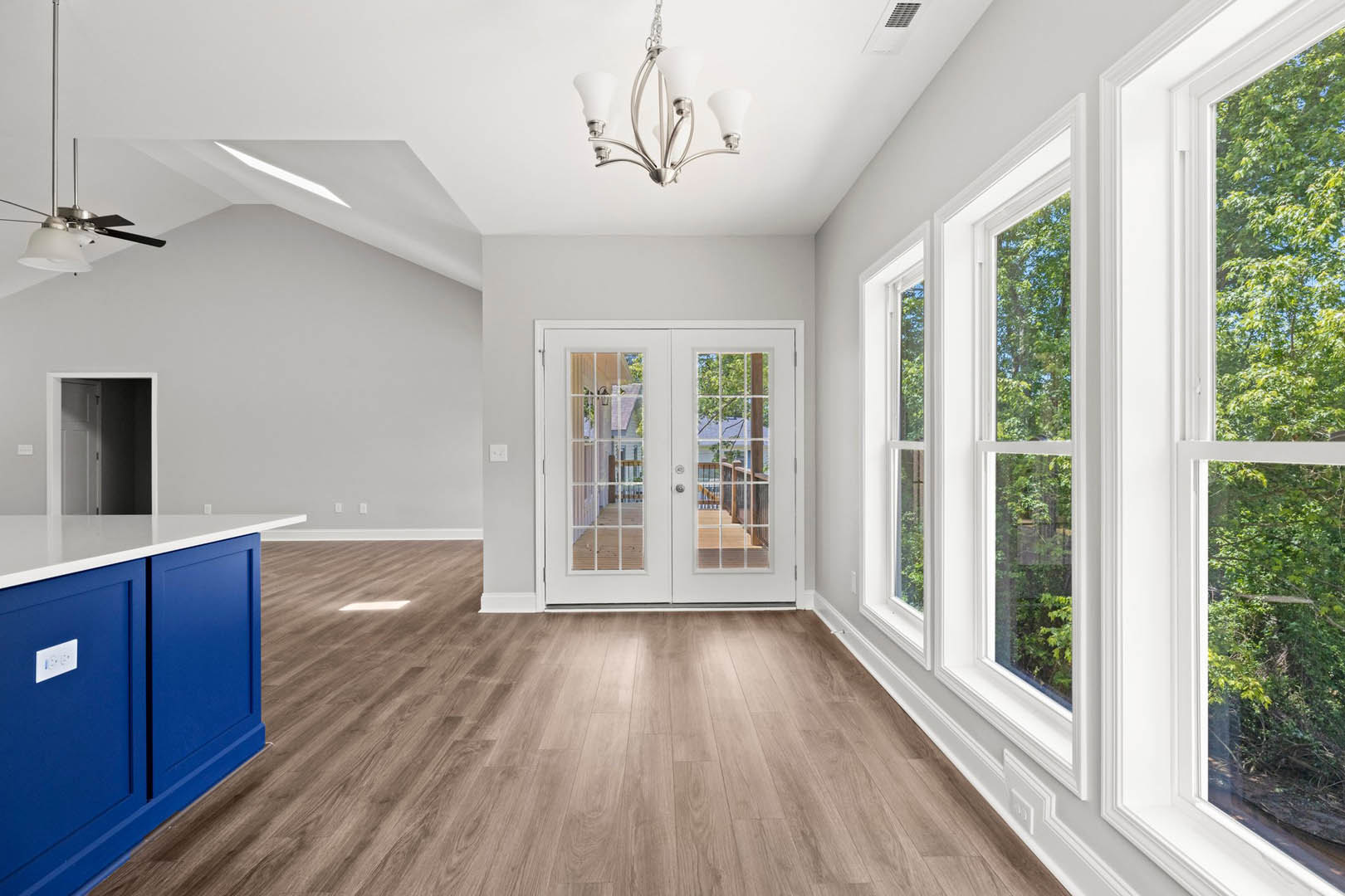 Wood floor and white walls in a room with double glass-paneled doors, blue accent wall with white outlet, blue cabinet, and chandelier.