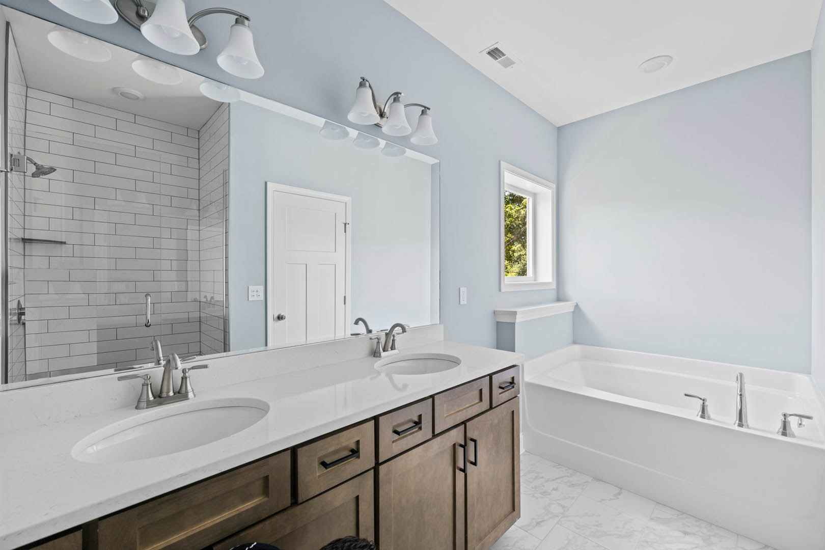 White tile bathroom featuring a freestanding bathtub with chrome faucets, a white sink and countertop beneath a wall mirror, a window with a white frame, and a white door with a
