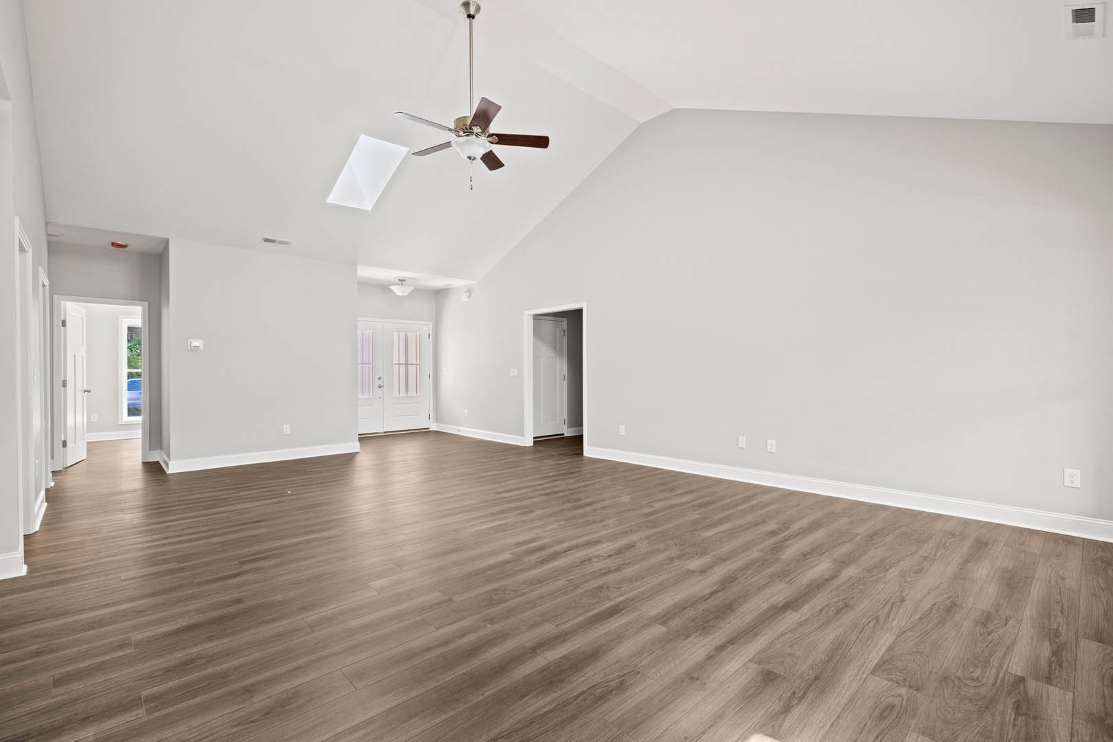Spacious room featuring wood flooring, white walls, ceiling fan with light fixture, white door with glass panels, square window with vent