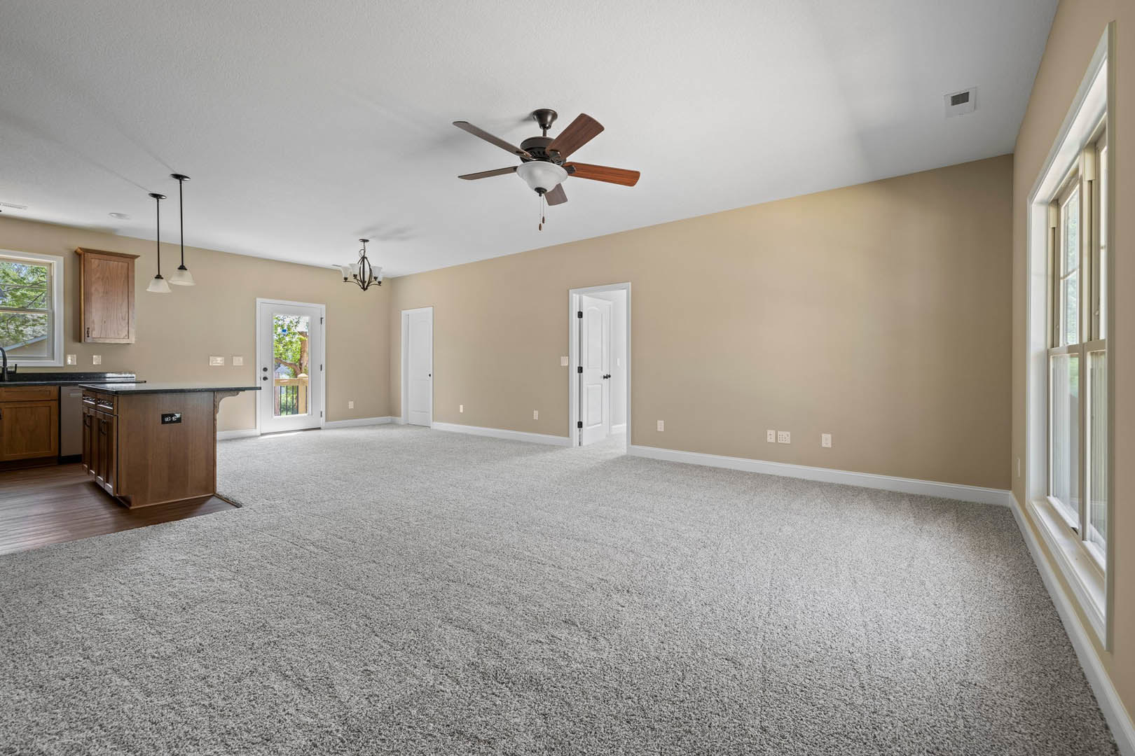 Carpeted room featuring a ceiling fan with light fixture, white door with black knobs, glass door with railing, and kitchen island with laminate countertop and cabinetry