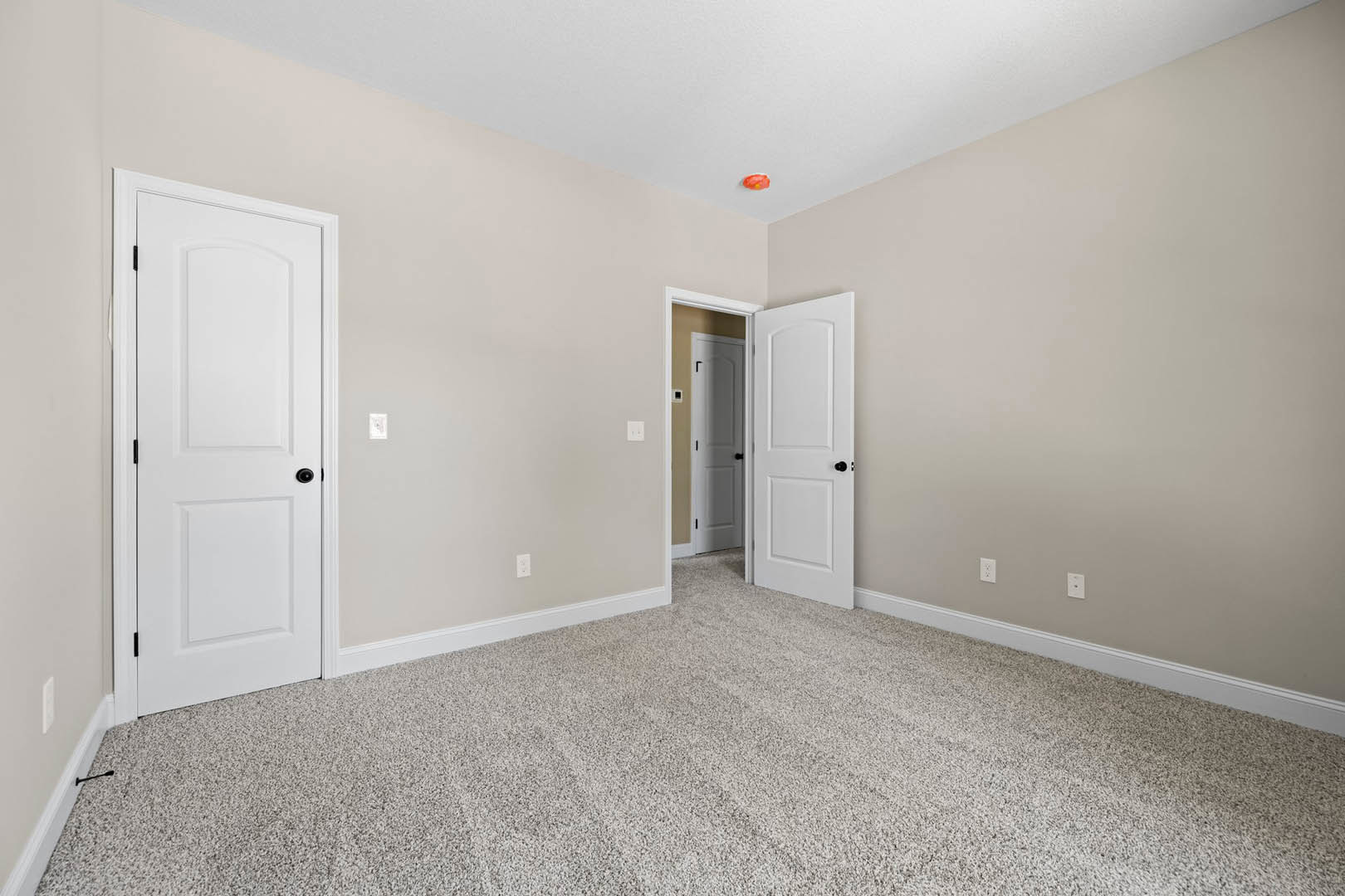 Carpeted room with white walls, white doors featuring black knobs, white ceiling, and wall outlets