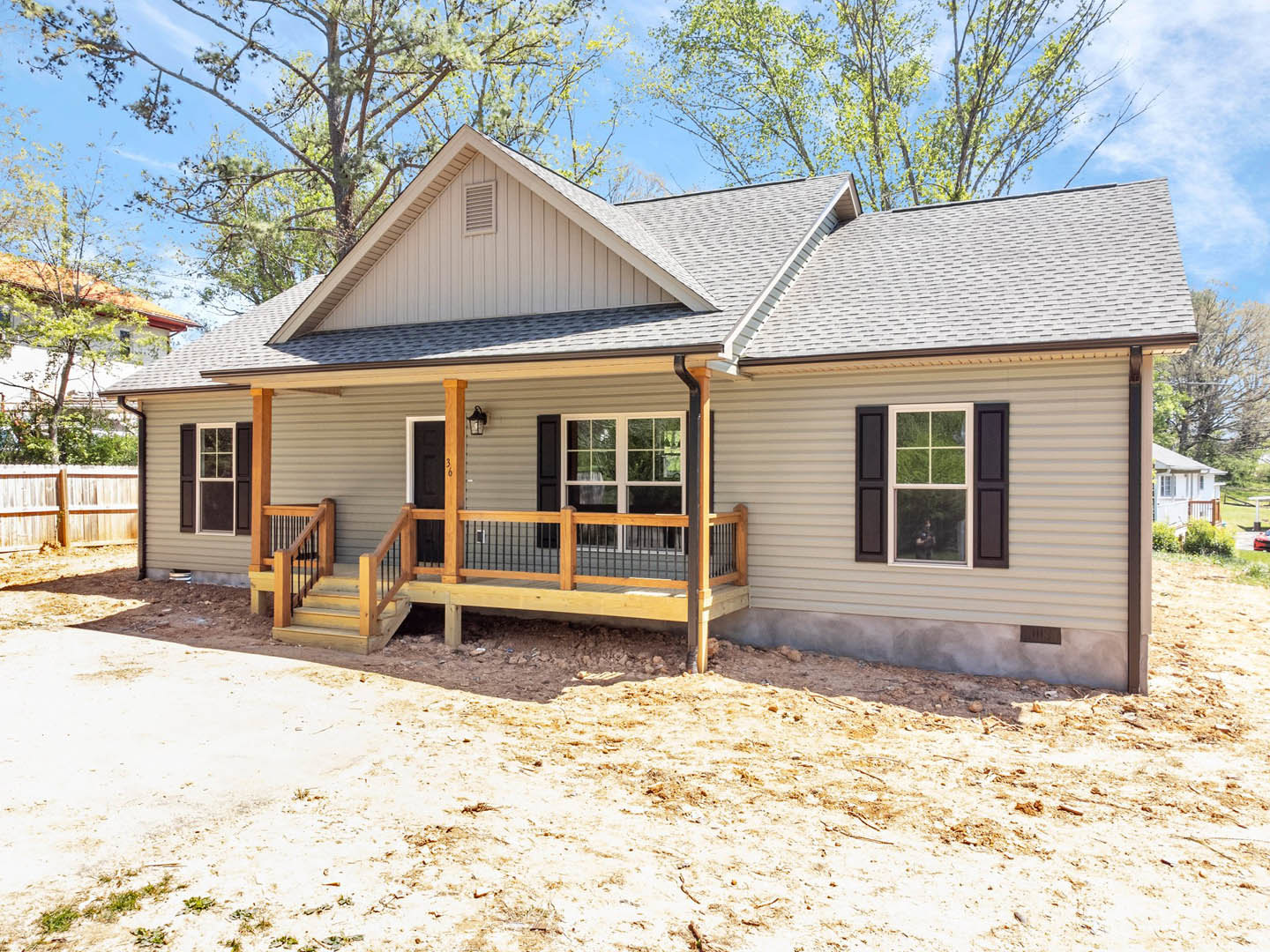 Two-story house with light siding, covered wooden porch featuring metal railing, concrete driveway, large windows, and mature tree in front yard