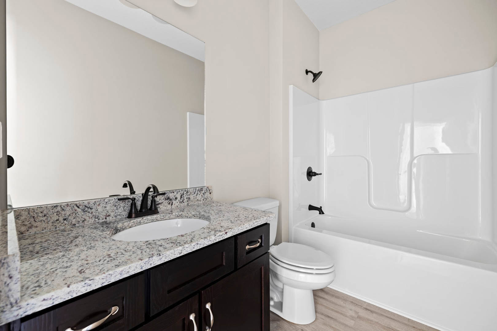 Bathroom with marble countertop, white sink with black border, white toilet beside a bathtub, light tile flooring, and neutral wall finishes.