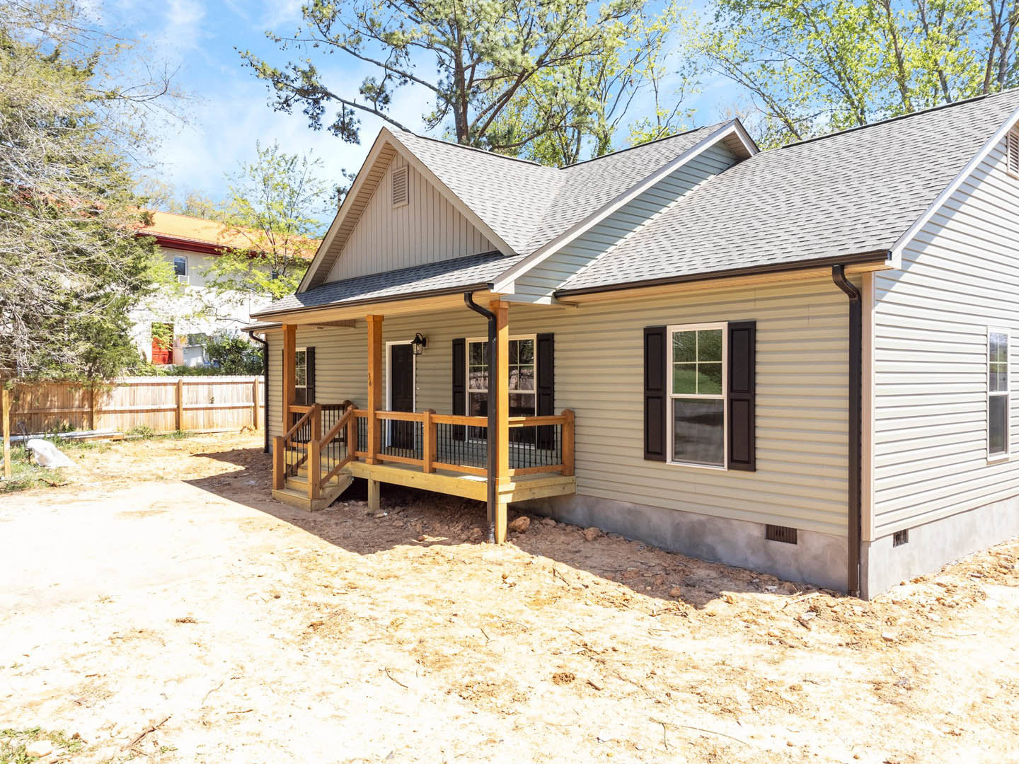Two-story house with white-trimmed windows, covered porch featuring wooden railing, wooden fence enclosing front yard, tree in background, white decorative object on lawn