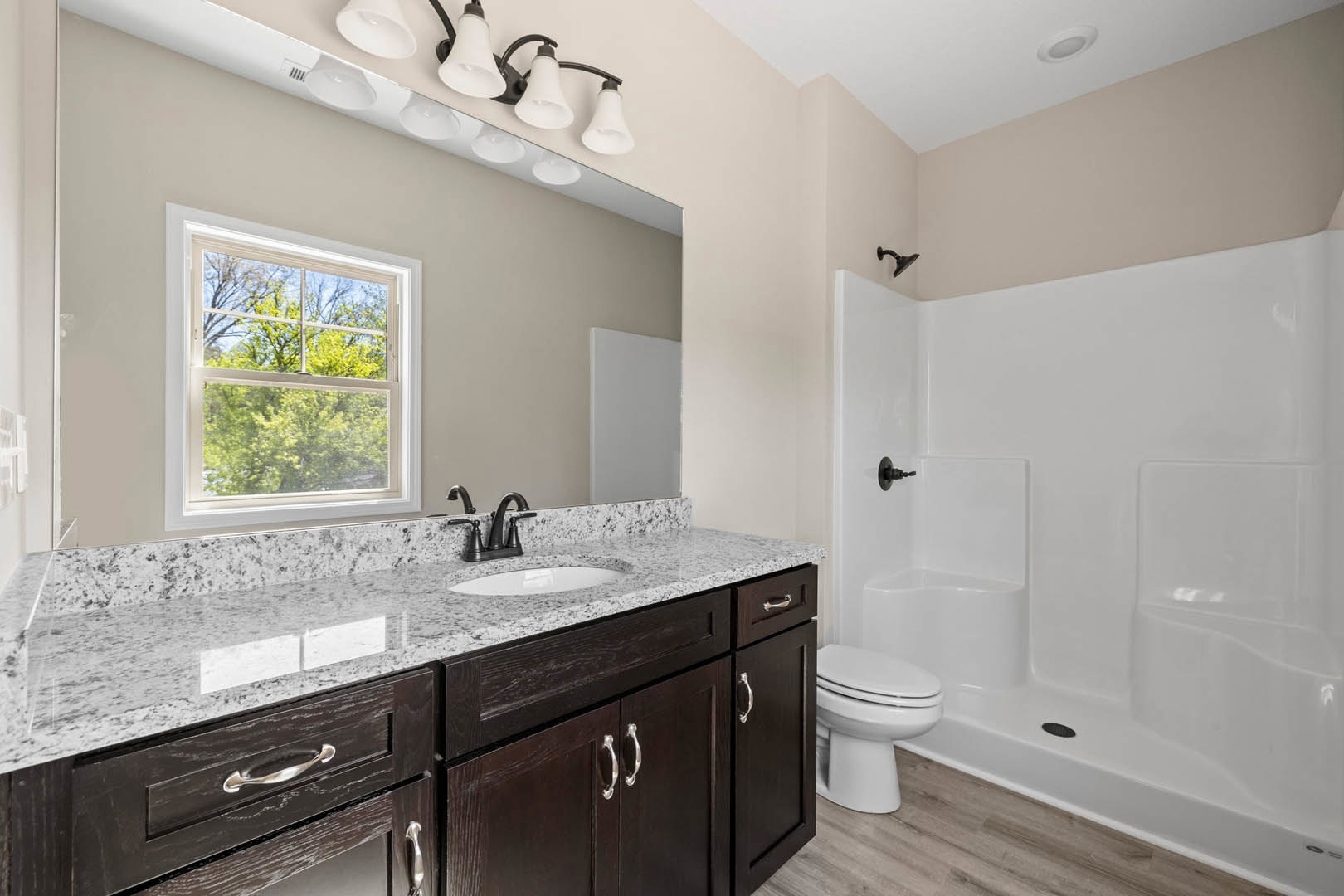 Modern bathroom featuring a white tile shower, built-in sink with chrome faucet, white toilet with closed lid, and a window overlooking green trees