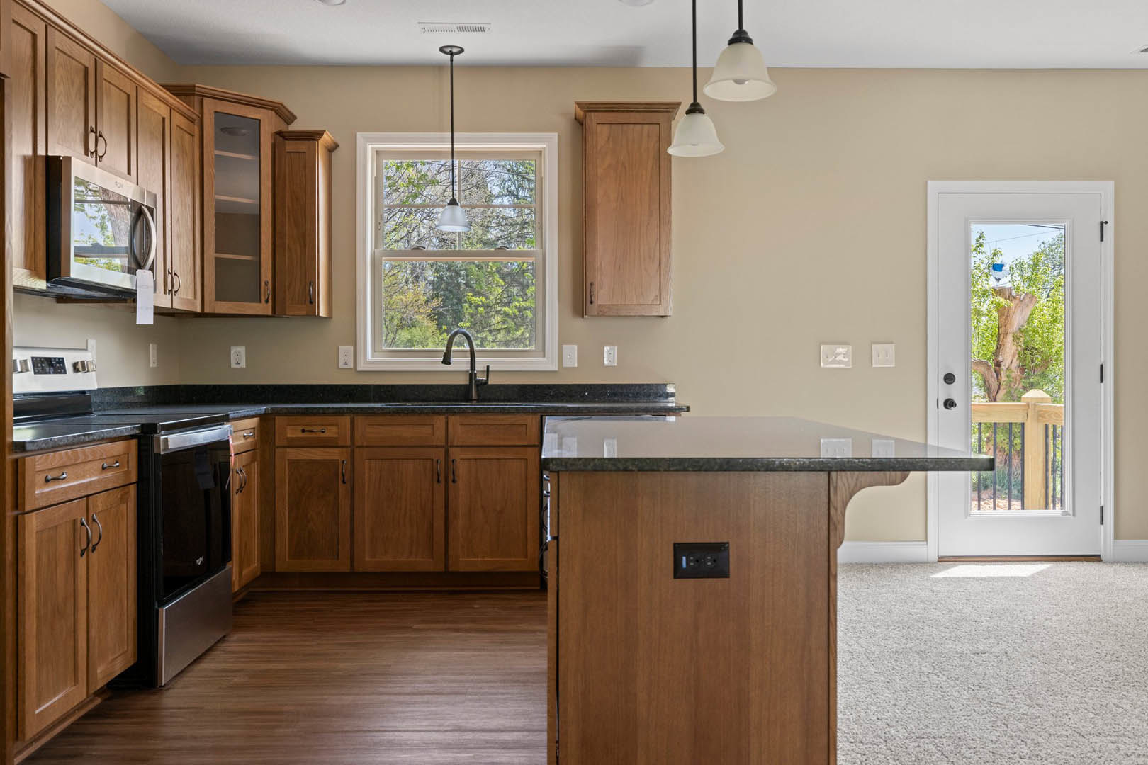 Kitchen with matte black stove, natural wood cabinets, stone countertop, stainless steel microwave, and windowed door with tree trunk visible outside