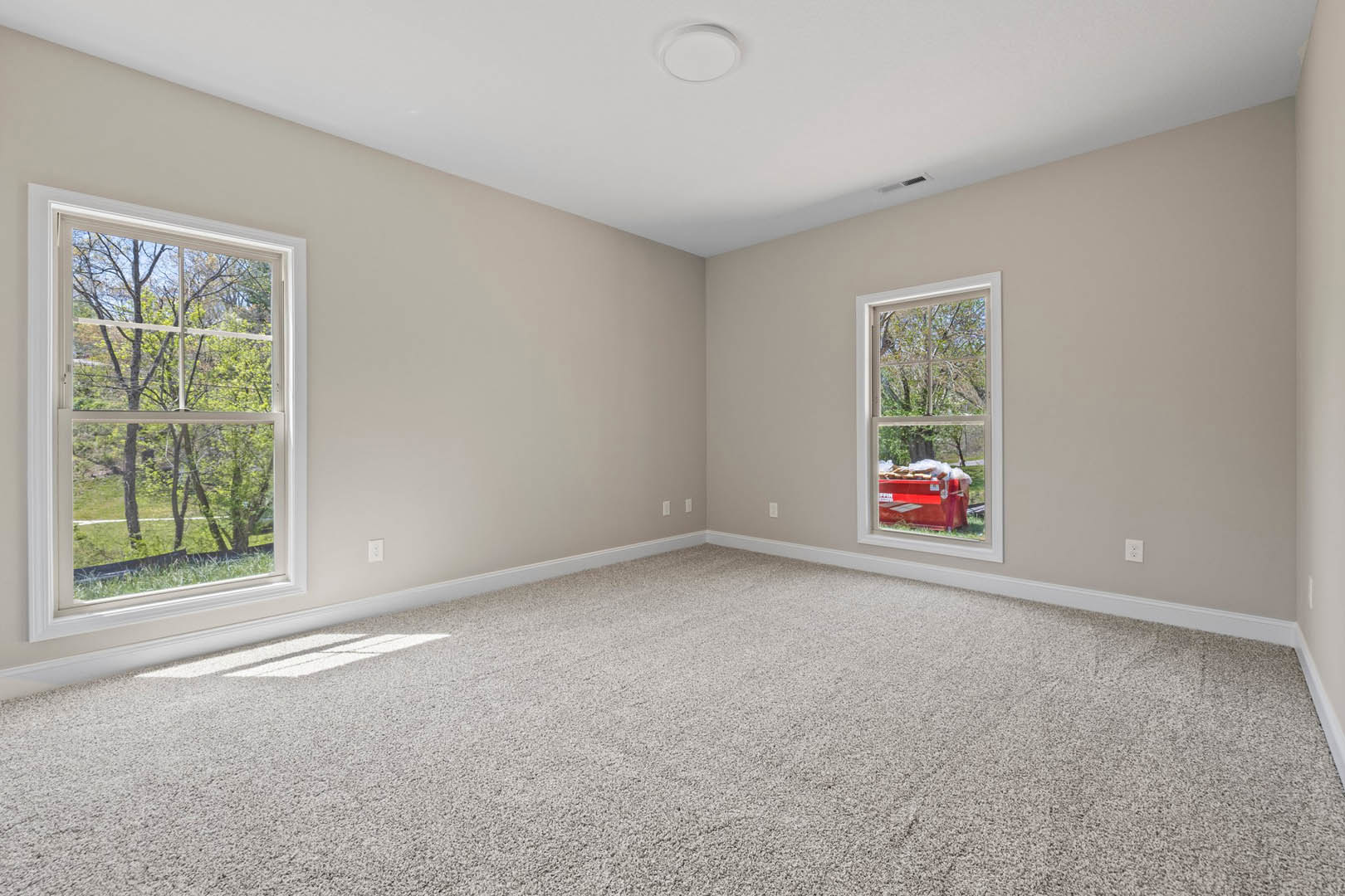 Room with two windows, carpeted walls, white ceiling with round light fixture, red bin with food, view of trees and picnic table outside