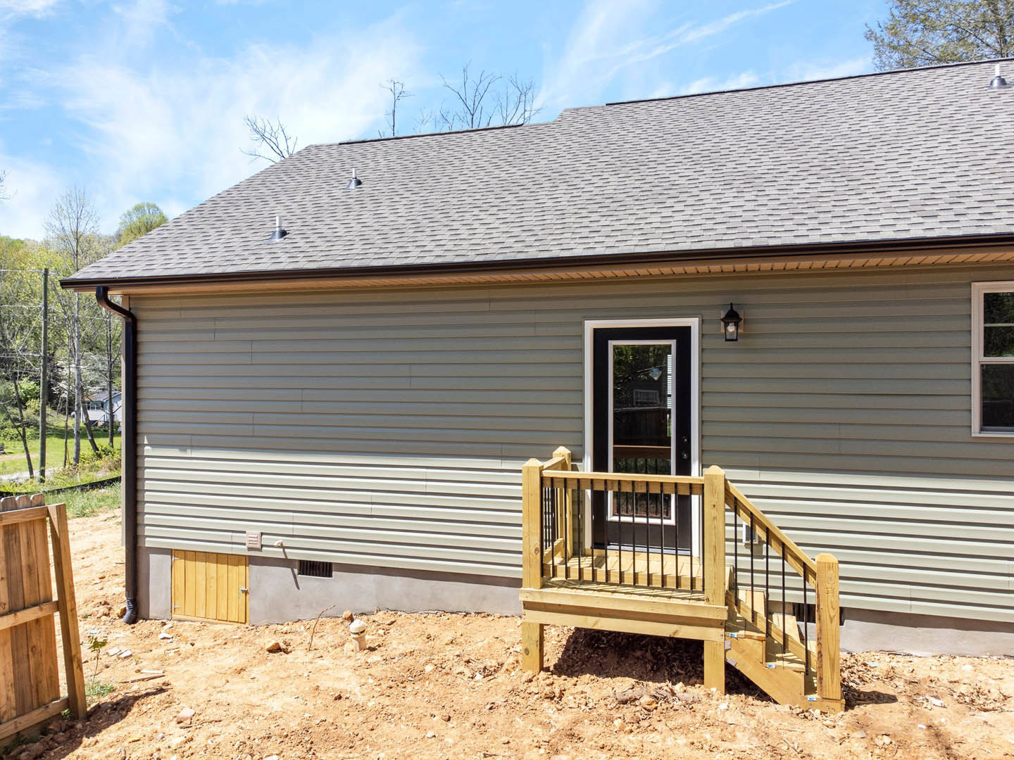 Wooden deck with stairs leading to a door, horizontal siding, large window, and fenced porch; roofline visible with trees in the background