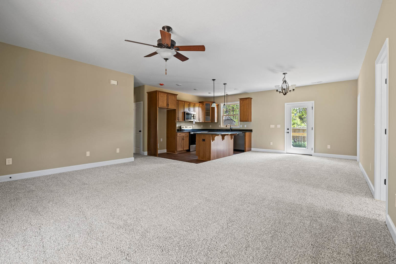 Open concept living room with carpet flooring, adjoining kitchen featuring a wooden bar counter, ceiling fan with light fixture, chandelier, white door with glass panel, and wood