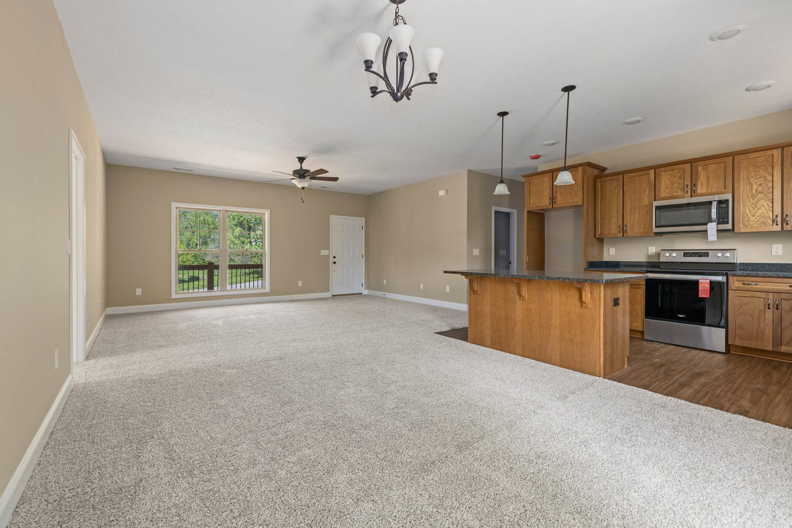 Open-concept living room with granite kitchen countertops, white cabinetry, stainless steel stove and microwave, dining area with chandelier, white door with black knobs, large