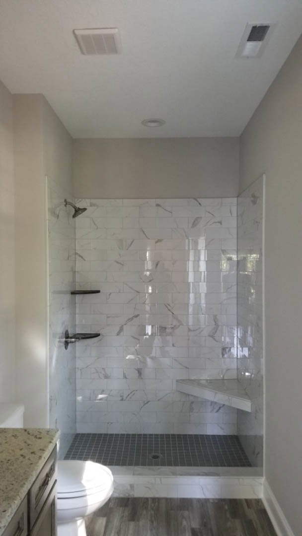 Walk-in shower featuring a marble wall, built-in shelf, and linear drain, adjacent to a wood-paneled accent wall and white vessel sink on a stone countertop.
