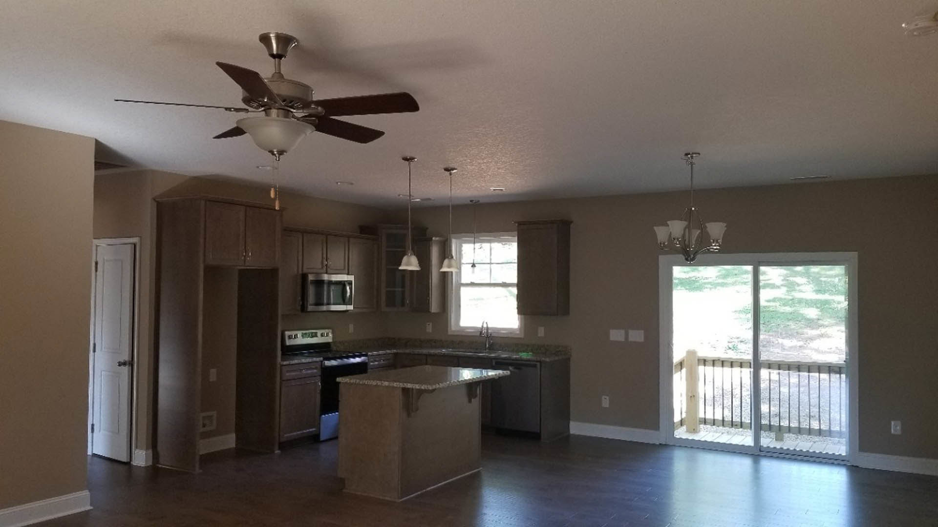 Kitchen with wood flooring, ceiling fan with light fixture, kitchen island featuring stone countertop, cabinetry, built-in microwave, sliding glass door with exterior railing, and