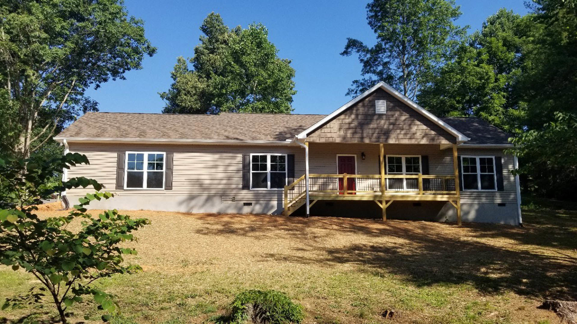 Two-story house with white-framed windows, covered front porch, wooden deck with railing, surrounded by trees and greenery.