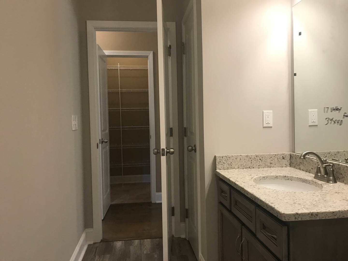 White bathroom with rectangular mirror above a modern sink, chrome faucet, tiled backsplash, wall outlet, and built-in shelving visible through open door.